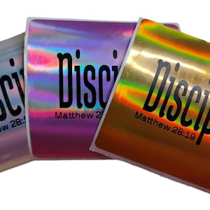 May include: Three holographic stickers with the word "Disciple" in black script. The stickers have a curved shape and feature the text "Matthew 28:19" or "Matthew 28:19". The stickers have a metallic sheen in shades of blue, purple, and gold.
