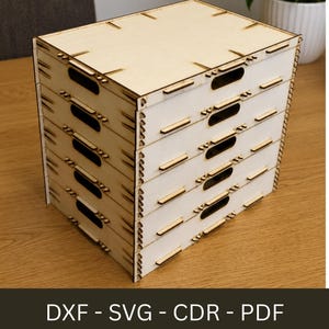 May include: A light-colored wooden storage box with five drawers. Each drawer has a rectangular handle cut-out. The box is constructed with interlocking pieces and features the text "DXF - SVG - CDR - PDF" at the bottom.
