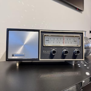 May include: A vintage Panasonic FM-AM Solid State radio. The radio features a silver speaker grill and a black and gold control panel. It has three knobs and a tuning dial. The Panasonic logo is displayed on the front.