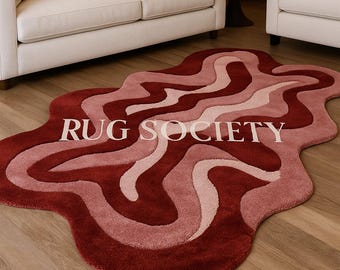 May include: A wavy, abstract rug in shades of red and pink, with the text "RUG SOCIETY" in white. The rug is placed on a wooden floor, with a white sofa and chairs in the background.