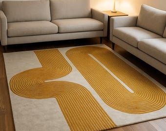May include: A rectangular area rug with a cream-colored background and a bold, abstract design in golden yellow. The pattern features curved, linear shapes that create a modern, geometric aesthetic. The rug is placed on a hardwood floor, with neutral-toned sofas in the background.