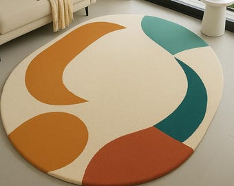 May include: An oval area rug with a cream-colored background and abstract shapes in shades of orange, teal, and rust. The rug is placed on a light gray floor in a living room setting.