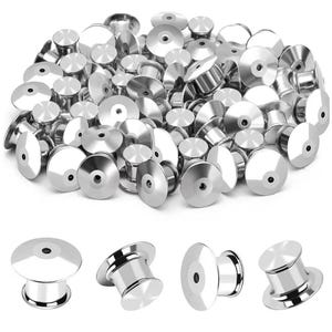 May include: A collection of shiny, silver-colored pin backs, with a flat, circular top and a cylindrical base. Several individual pin backs are shown below the main pile. These jewelry findings are used to secure pins.