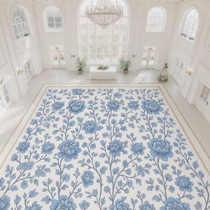 Op de afbeelding: Een bovenaanzicht van een grote, sierlijke kamer met een bloemenkleed. Het kleed heeft een herhalend patroon van blauwe bloemen en ranken op een crèmekleurige achtergrond. De kamer heeft witte muren, grote ramen en een kristallen kroonluchter.