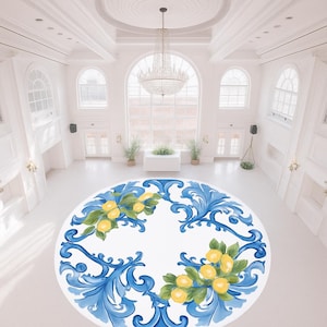 以下が含まれることがあります： 白を背景に、青と黄色のレモン柄が描かれた大きな円形ラグ。明るい白い部屋にあり、大きな窓とシャンデリアがあります。デザインはレモンと葉が特徴です。