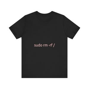 Puede incluir: Camiseta negra con el texto "sudo rm -rf /" en rosa. La camiseta de manga corta tiene cuello redondo y está hecha de un tejido suave. El texto está centrado en la parte delantera.
