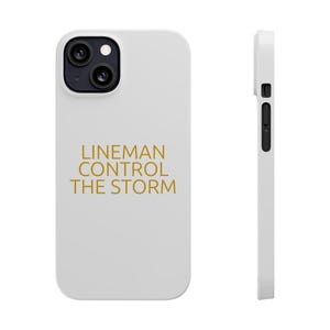 Puede incluir: Funda de teléfono blanca con el texto dorado "LINEMAN CONTROL THE STORM". La funda tiene un módulo de cámara negro y botones laterales. La imagen muestra la parte delantera y lateral de la funda.