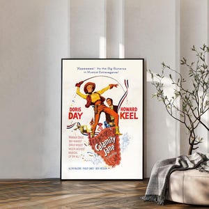 Puede incluir: Un póster de película vintage de Calamity Jane con Doris Day y Howard Keel. La ilustración muestra a una figura central con camisa amarilla y pantalones naranjas sosteniendo un lazo, con el título Calamity Jane en un marco rojo decorativo.