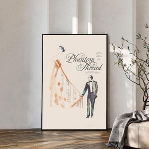 May include: A framed poster featuring a watercolor illustration of a person in a flowing peach gown standing on a staircase next to a person in a dark suit. The text Phantom Thread is printed in black script, with additional cast and director credits.