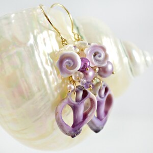 May include: Purple and white shell earrings with gold hoops. The earrings feature a cluster of small shells, pearls, and beads.