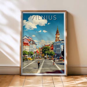 Puede incluir: Póster de viaje enmarcado de Vilna, Lituania, que representa una plaza de la ciudad con edificios, árboles y personas. El póster tiene un cielo azul con nubes y la palabra "VILNIUS" en la parte superior.