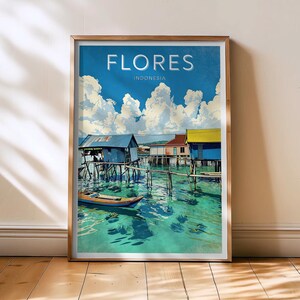 May include: A framed print featuring a vibrant illustration of Flores, Indonesia. The artwork depicts colorful stilt houses over turquoise water, a small boat, and a bright blue sky with fluffy white clouds. The word "FLORES" is printed at the top.