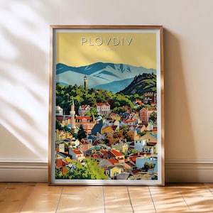 May include: A framed art print featuring a colorful illustration of Plovdiv, Bulgaria. The artwork depicts a cityscape with buildings of various colors, a mountain range, and the text "Plovdiv Bulgaria" at the top. The print is displayed on a wooden floor.