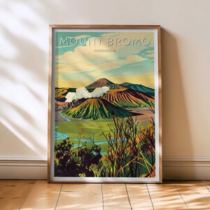 Könnte beinhalten: Ein gerahmter Kunstdruck von Mount Bromo in Indonesien. Die Illustration im Vintage-Stil zeigt eine lebendige Landschaft mit einem Vulkan, grünen Hügeln und einem Fluss. Der Text "MOUNT BROMO" und "INDONESIA" ist oben zu sehen.