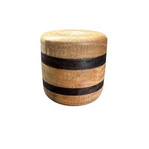 May include: A cylindrical wooden object with a flat top and bottom. The light-colored wood is accented by two dark brown bands. The object is likely a decorative element or a small container.