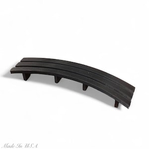 May include: A curved, black metal bench with three horizontal slats and three supporting legs. The bench is made in the USA and is set against a white background. The bench is a decorative item.