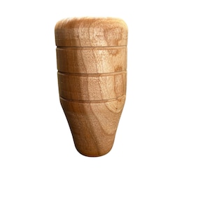 Puede incluir: Un pomo de madera de color claro con una parte superior redondeada y una base cónica. El pomo tiene tres ranuras horizontales y un patrón de vetas de madera natural. El objeto está aislado sobre un fondo blanco.