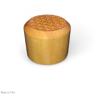 Puede incluir: Objeto cilíndrico de madera con acabado marrón claro. La superficie superior presenta un patrón de panal tallado. Es probable que el artículo sea una pieza decorativa o funcional, posiblemente un tapón o un recipiente pequeño.