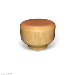 May include: A wooden bottle stopper with a light brown top and a light tan body. The stopper has a rounded top and a flared base. The wood grain is visible on the sides of the stopper.
