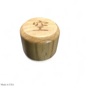 May include: A cylindrical wooden bottle stopper with a light brown finish. The top of the stopper features a carved Japanese character. The stopper is made of wood and has a smooth, polished surface.
