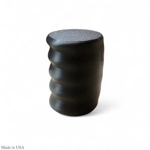 May include: A black, cylindrical object with a textured, gray top and a ridged, curved body. The object is set against a white background. The text "Made in USA" is at the bottom left.
