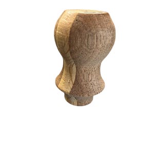 May include: A turned wooden furniture leg with a bulbous top and a flared base. The wood has a natural, light brown color with visible grain, and the leg is unfinished.