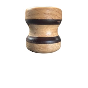 May include: A wooden bottle stopper with a light brown and dark brown striped design. The stopper has a rounded top and bottom with a slightly hourglass shape. The wood grain is visible.