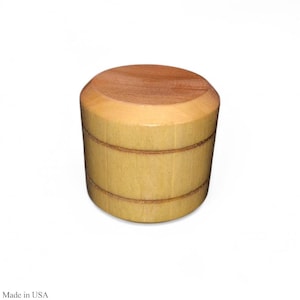May include: A cylindrical wooden object with a light brown body and a darker brown top. The body has two horizontal grooves. The text "Made in USA" is at the bottom.