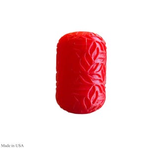 May include: A vibrant red, cylindrical object with a carved leaf pattern. The object is a solid color and has a smooth, glossy finish. The item is made in the USA.