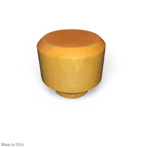 May include: A wooden bottle stopper with a light brown top and a light yellow body. The stopper has a cylindrical shape with a slightly tapered body and a small base. The top is a darker shade of brown than the body.