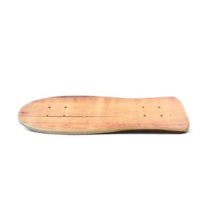 Könnte beinhalten: Ein hellbraunes Skateboard-Deck aus Holz mit abgerundeter Nase und abgerundetem Heck. Das Deck hat ein natürliches Holzmaserungsmuster und vorgebohrte Löcher zur Montage von Trucks. Das Skateboard-Deck ist etwa 76 cm lang.