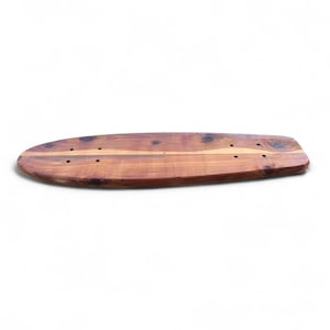 Könnte beinhalten: Ein Skateboard-Deck aus Holz mit natürlicher Holzmaserung. Das Deck ist oval geformt und hat vorgebohrte Löcher zur Montage der Achsen. Das Holz hat einen warmen, rötlich-braunen Farbton mit sichtbaren Knoten und Maserungsmustern. Das Skateboard-Deck ist etwa 76 cm lang.