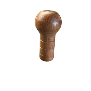 May include: A wooden shift knob with a rounded top and a cylindrical base. The knob is made of a dark brown wood and has a smooth, polished finish. The base has several horizontal grooves.