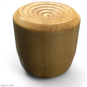 May include: A cylindrical wooden bottle stopper with a light brown finish. The top features a concentric circular grain pattern. The base is slightly wider than the top. The text "Made in USA" is visible at the bottom.