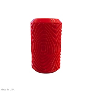 May include: A vibrant red cylindrical tool with a textured surface, featuring a repeating concentric pattern resembling wood grain. The tool is designed for creating decorative patterns on various surfaces. The item is made in the USA.