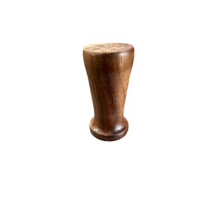 May include: A solid, dark brown wooden bottle stopper with a flared, conical shape. The top is flat and circular, while the base is rounded. The wood grain is visible, adding texture to the piece. This stopper is designed to fit into a bottle.