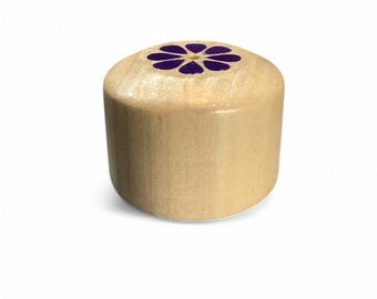 May include: A cylindrical wooden bottle stopper with a purple flower design on top. The stopper is made of light-colored wood and is suitable for wine bottles. The text "Made in USA" is printed at the bottom.
