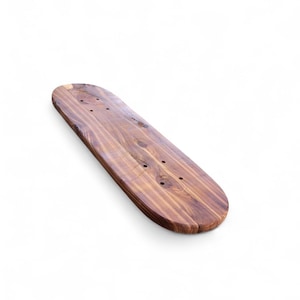Könnte beinhalten: Ein Skateboard-Deck aus Holz mit natürlicher Holzmaserung. Das Deck hat eine abgerundete Form mit vorgebohrten Löchern zur Montage von Trucks. Das Holz hat eine warme braune Farbe.