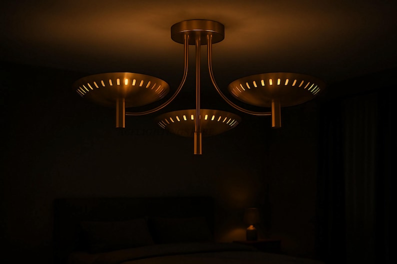 Puede incluir: Un plaf&oacute;n de techo de tres luces con un acabado dorado c&aacute;lido. La l&aacute;mpara tiene tres pantallas en forma de cuenco con bordes ranurados, suspendidas de brazos curvos. La l&aacute;mpara est&aacute; montada en un techo, con un fondo oscuro.