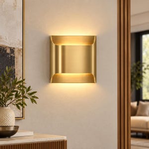 May include: A square wall sconce with a brushed gold finish, featuring a curved metal design that directs light both upward and downward, creating a warm glow against the wall surface while maintaining a clean and symmetrical geometric shape.