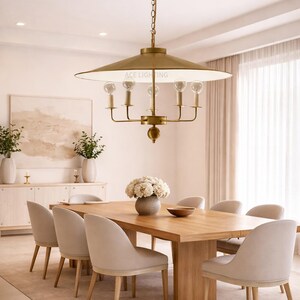 May include: A dining room scene featuring a large wooden table surrounded by upholstered chairs. Above the table hangs a brass chandelier with exposed light bulbs. The room is decorated in neutral tones with a rug and artwork.