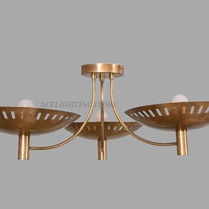 May include: A brass-toned ceiling light fixture with three bowl-shaped shades. Each shade has a series of evenly spaced, angled cutouts. The fixture has a central stem and curved arms supporting the shades. The text "ACELIGHTINGSTORE" is visible.