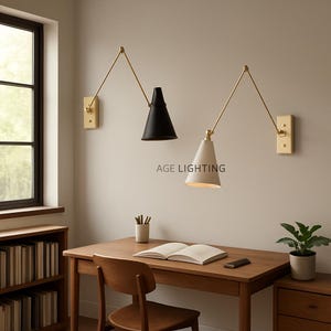 May include: Two wall-mounted lamps with adjustable arms. One lamp has a black conical shade, the other is white. Both have gold-colored arms and rectangular wall mounts. The text "AGE LIGHTING" is printed on the wall.