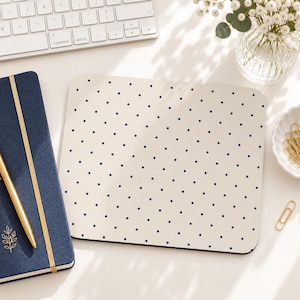 May include: A rectangular mouse pad featuring a cream-colored surface with a repeating pattern of small, dark navy blue polka dots. The mouse pad has rounded corners and a smooth, flat texture, providing a clean and simple aesthetic for a workspace.