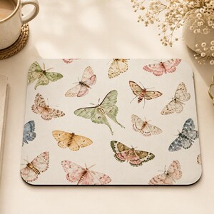May include: A square mouse pad featuring a repeating pattern of various moths and butterflies in soft pastel shades of green, pink, yellow, and blue on a cream-colored background. The design includes a prominent central green moth.