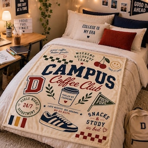 May include: A cream-coloured throw blanket featuring a collegiate-style graphic print with the text CAMPUS Coffee Club, a coffee cup, a sneaker, cherries, and various phrases including Weekend Recovery Team, Girls Night, and Focus Fuel.