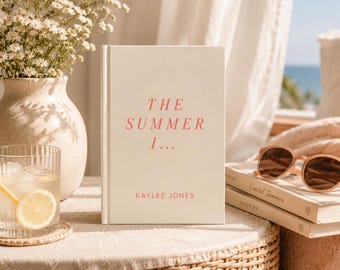 May include: A hardcover book with a cream-colored cover featuring the pink text THE SUMMER I... and KAYLEE JONES. The book stands upright next to a glass of water with a lemon slice, a vase of white flowers, and a pair of brown sunglasses on books.