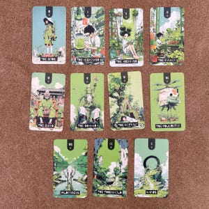 May include: A set of ten rectangular tarot-style cards featuring green-toned illustrations. Each card displays a unique character or landscape scene with a Roman numeral and a title, including The Spore, The Alchemist, The Archivist, The Farmer, The Elder, The Shaman, The Biophile, The Pollinator, Wilderness, The Threshold, and Kairos.