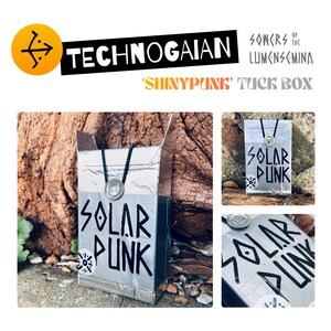 May include: A silver-colored rectangular tuck box featuring the text 'SOLAR PUNK' in bold black lettering. The box is adorned with a circular metallic emblem and a black cord detail. The design includes a small circular graphic icon.
