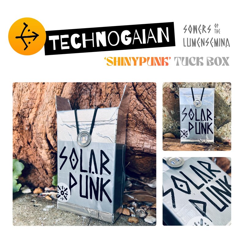 May include: A silver-colored rectangular tuck box featuring the text 'SOLAR PUNK' in bold black lettering. The box is adorned with a circular metallic emblem and a black cord detail. The design includes a small circular graphic icon.